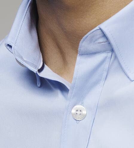 Ribetes en color blanco y azul marino en el interior del cuello y botones de n&aacute;car en relieve t&iacute;picos de Lacoste.